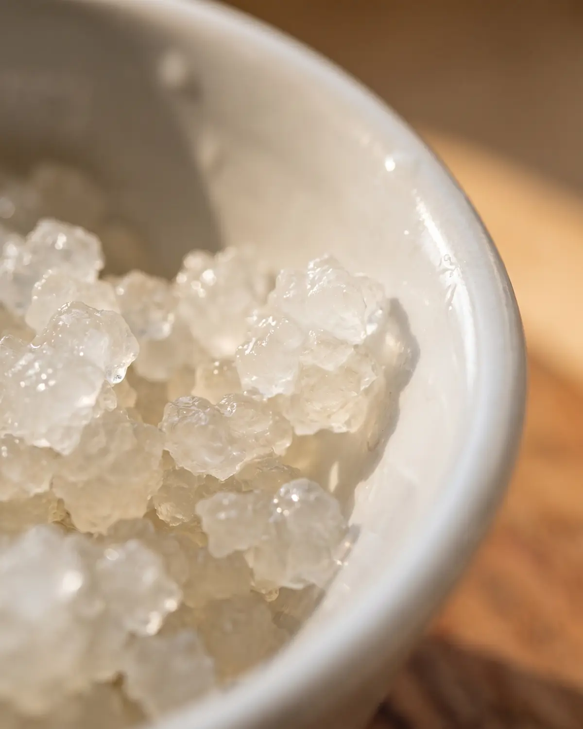 tweede fermentatie waterkefir Macrobeeld van gelatineachtige waterkefirkorrels tegen nat wit keramiek, met doorschijnende structuur.
