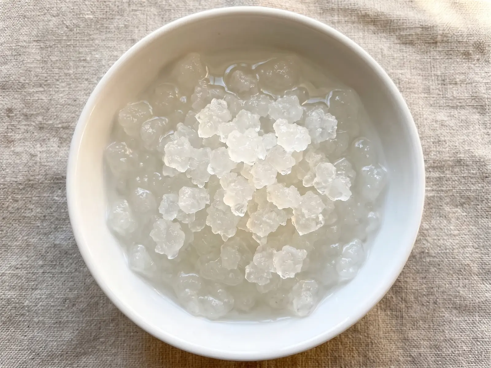water kefir drink Doorschijnende waterkefirkorrels in een witte kom op ruw linnen met helder water en bovenlicht.
